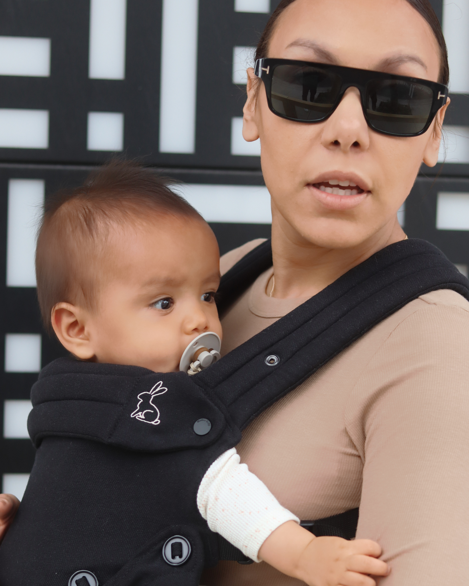 Mom wearing ergonomic black baby carrier with baby outdoors
