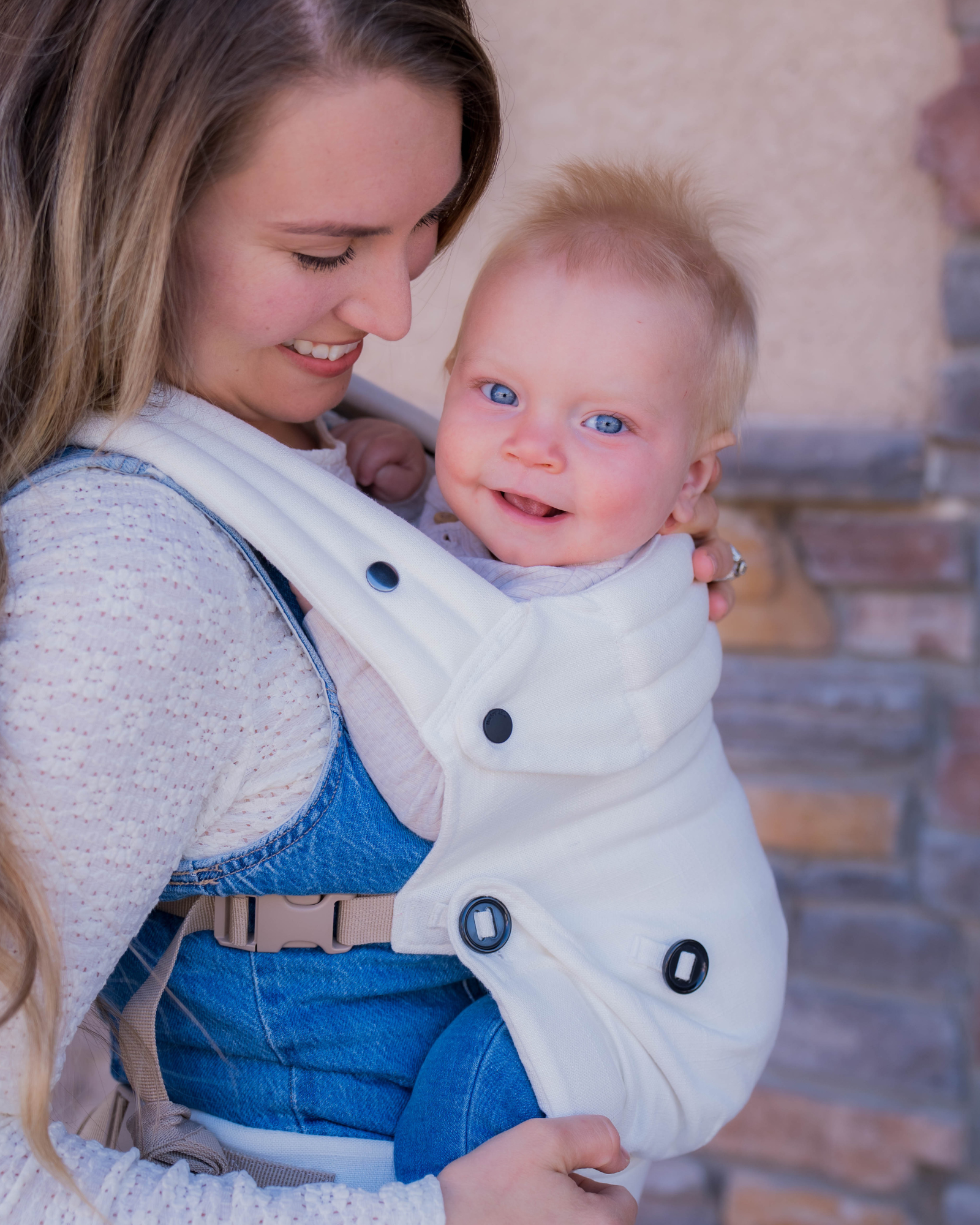 Mom wearing ergonomic cream baby carrier with baby outdoors