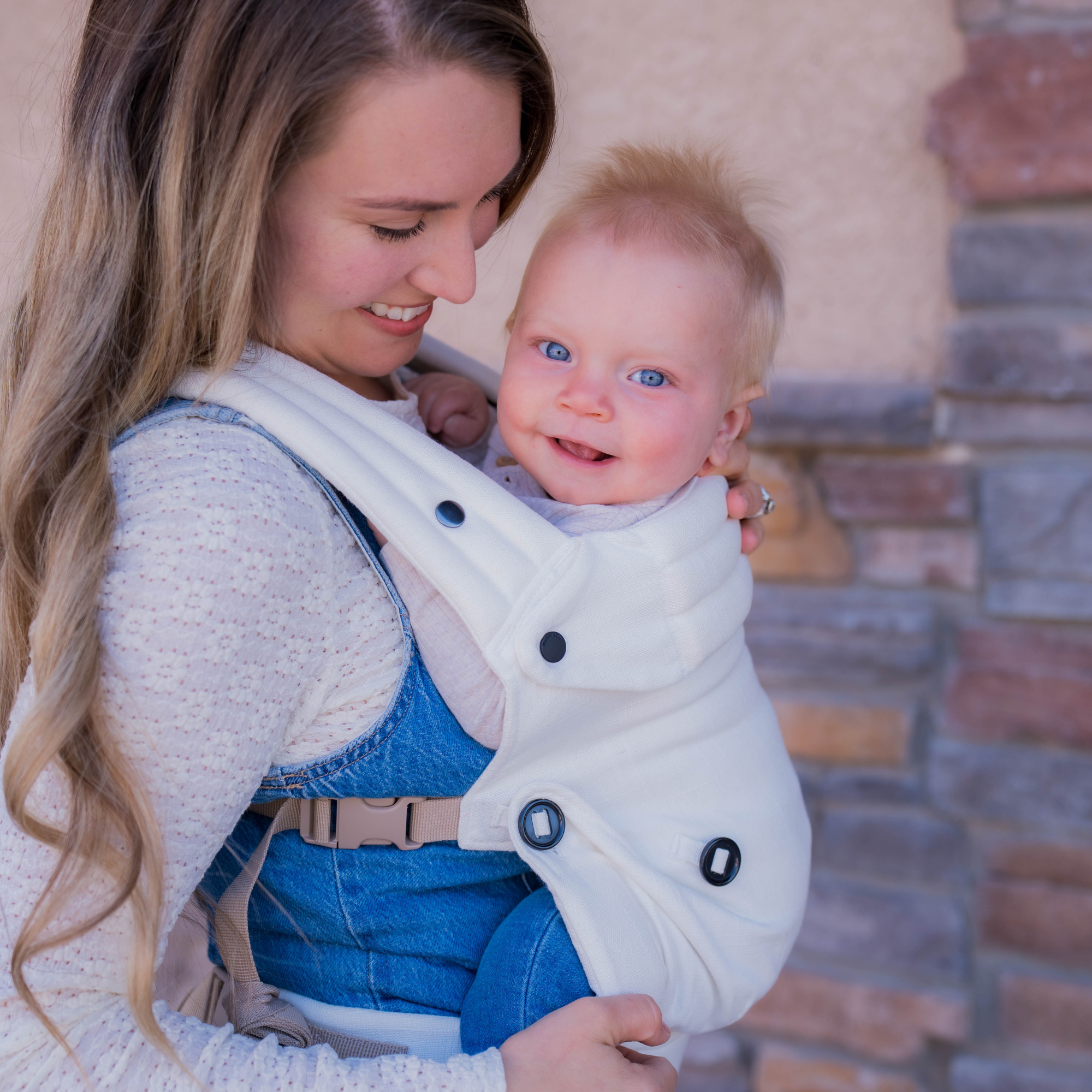 Mom wearing ergonomic cream baby carrier with baby outdoors