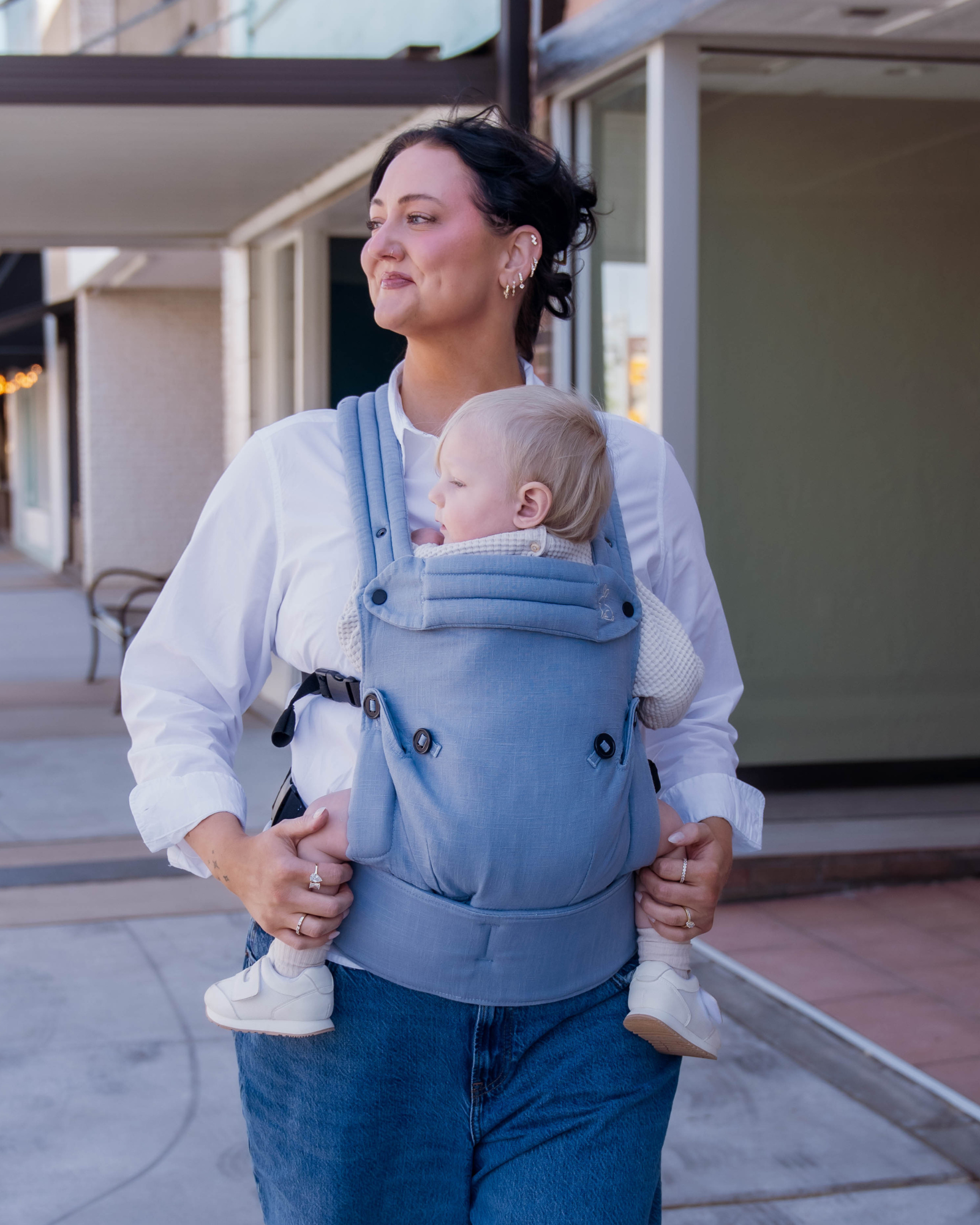 Mom wearing ergonomic blue baby carrier with baby outdoors