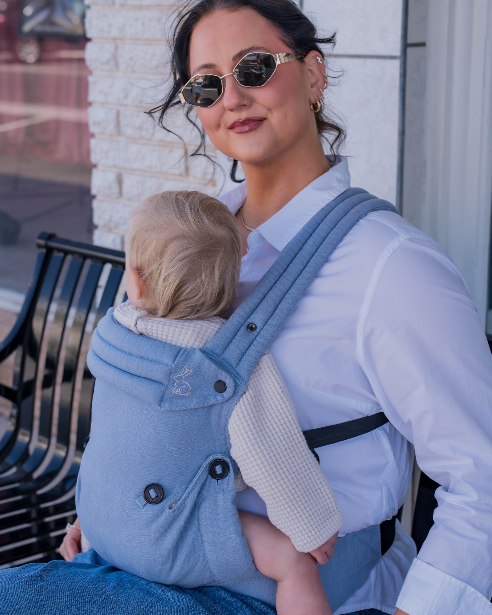 Mom wearing blue baby carrier with baby outdoors