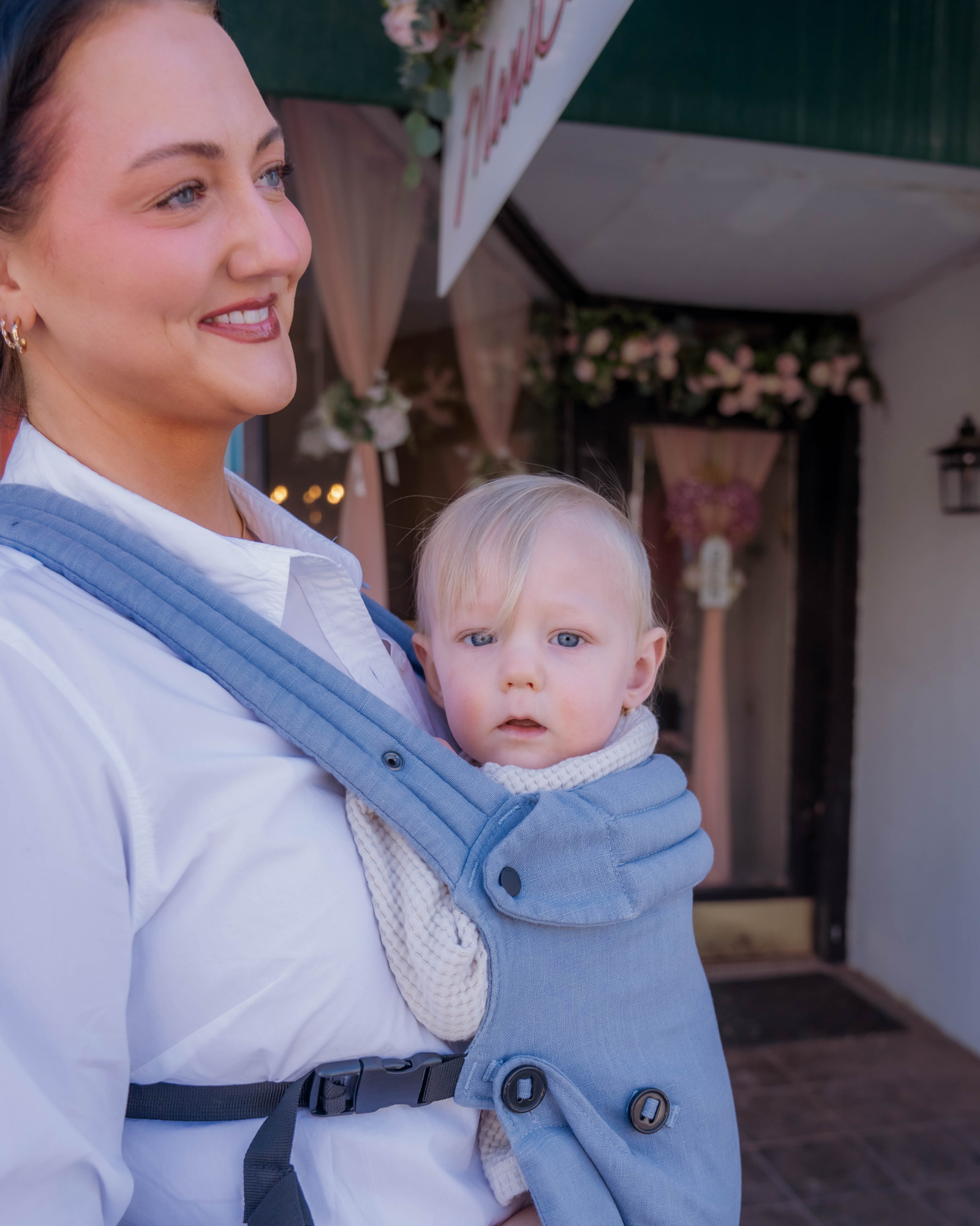 Mom wearing ergonomic blue baby carrier with baby while shopping