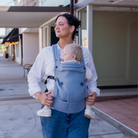 Mom wearing ergonomic blue baby carrier with baby outdoors